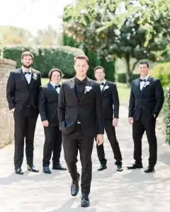 Groom in black wedding suit walking in front of his groomsmen who are wearing matching black wedding suits 
