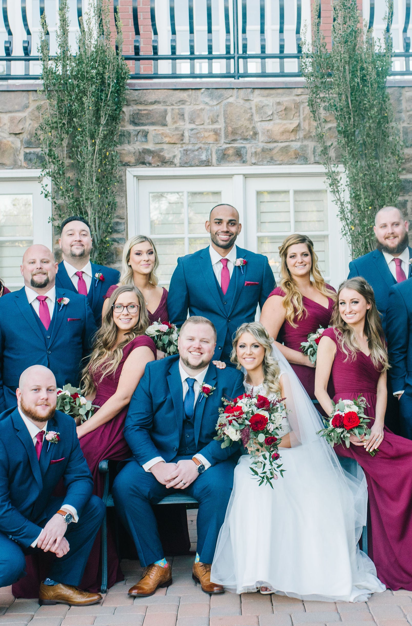 A bridal party wearing maroon wedding colors poses outside