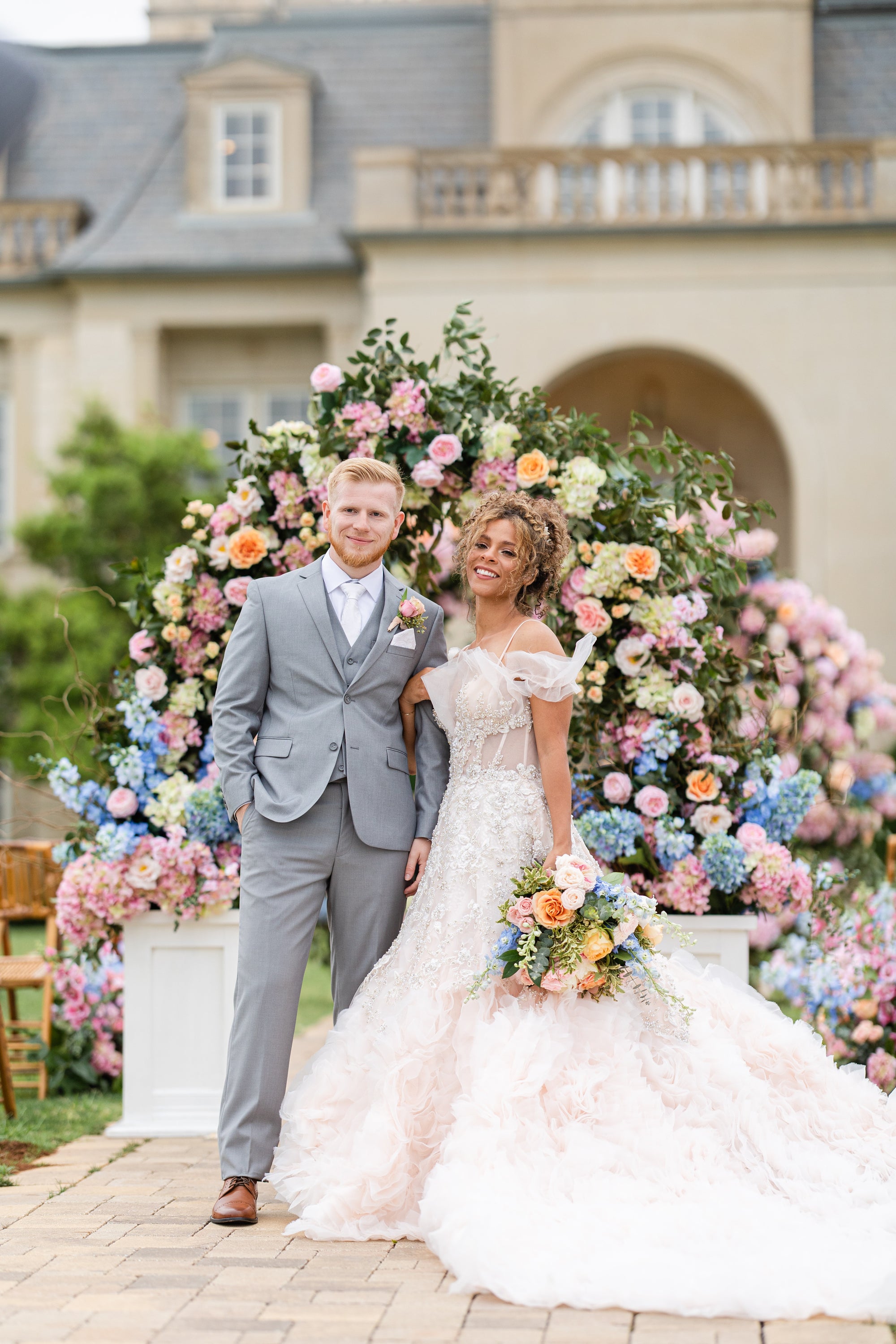 A happy bride and groom pose in front of an extravagant flower arch as part of their spring wedding theme