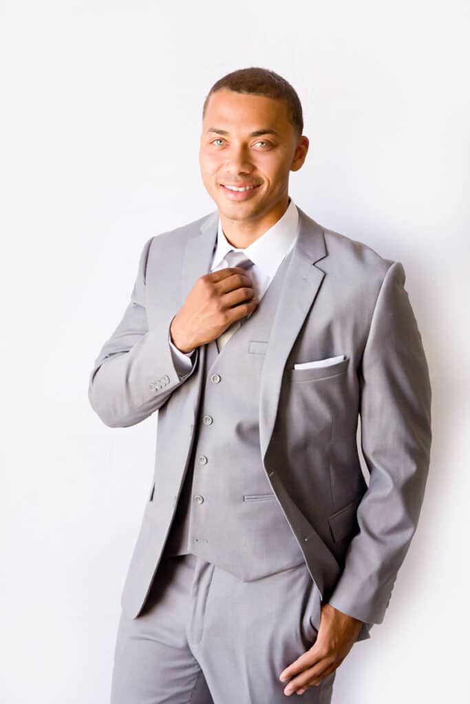 A man in a Modern Groom light-gray suit poses.