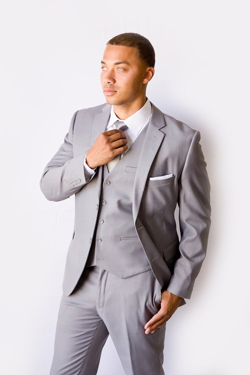 Man adjusting his tie in a light grey modern groom suit.
