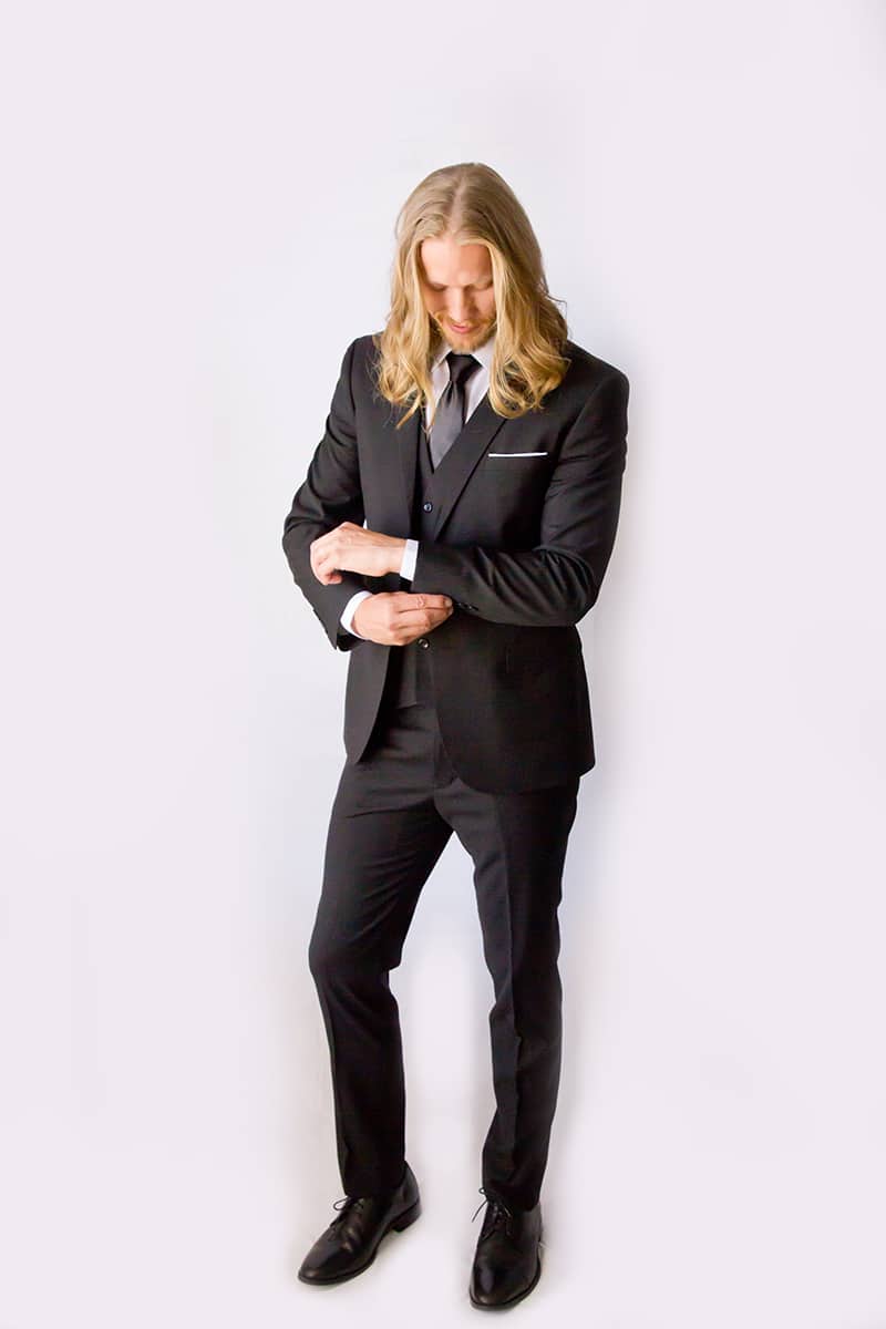 Male model in a black suit adjusting his cuffs.