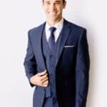 A young male model smiles while showing off Modern Groom's blue suit jacket.