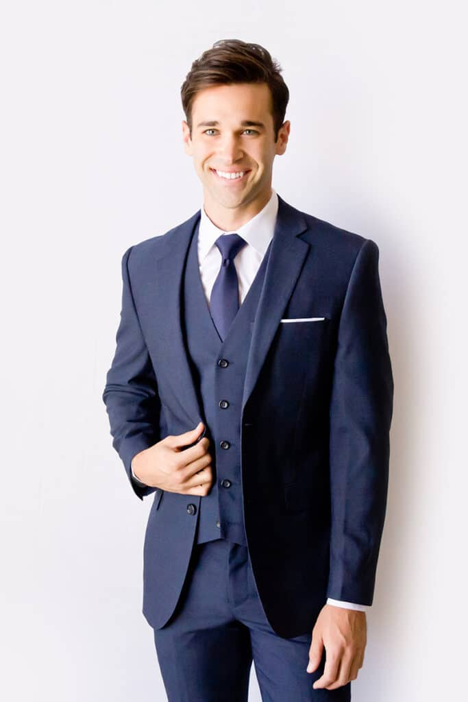 A young male model smiles while showing off Modern Groom's blue suit jacket.