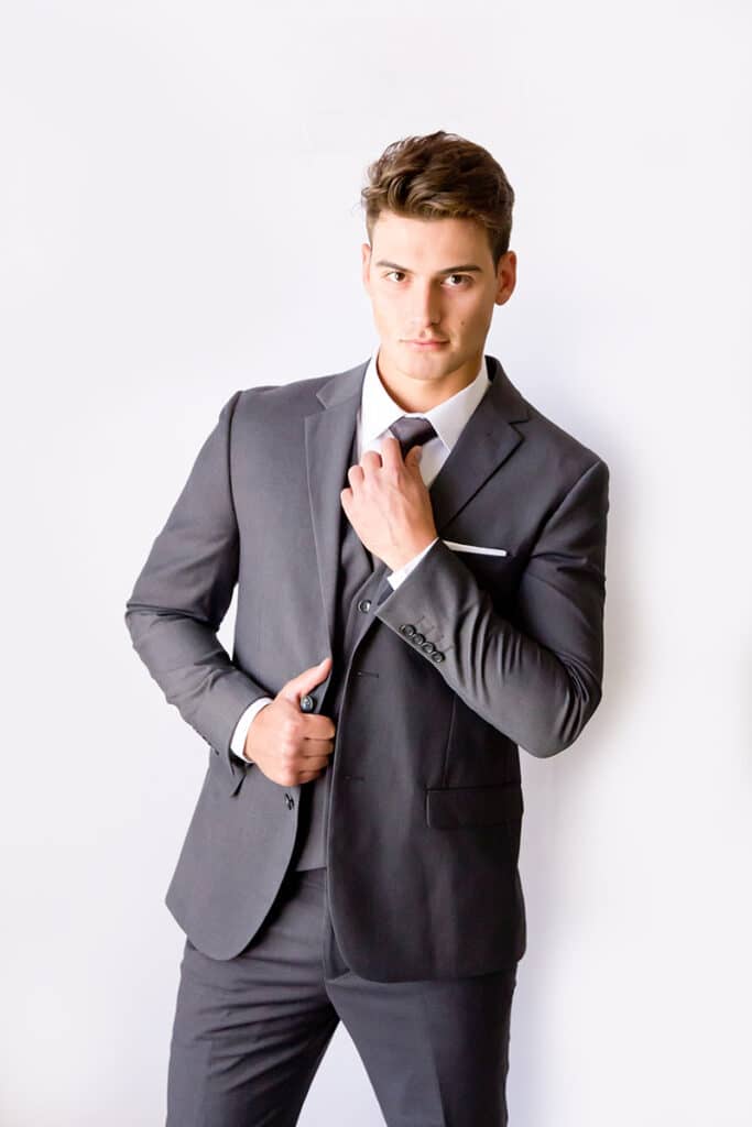 A man adjusts his tie as he poses in a gray wedding suit.