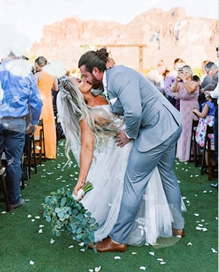 bride and groom in heathered grey wedding suit kiss in front of their wedding guests