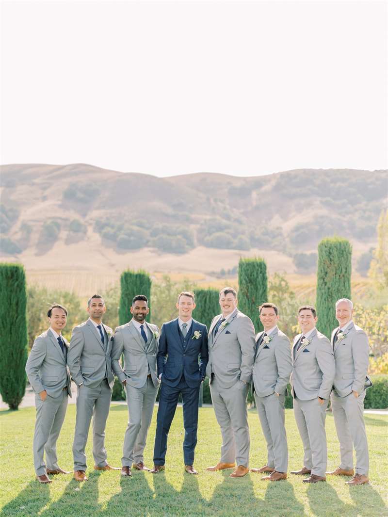 A groom in a navy suit poses with his groomsmen in light gray suits.