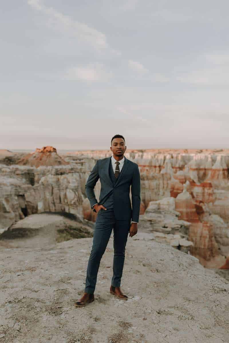 A man poses in a canyon wearing a dark gray suit.