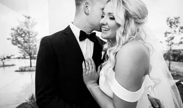 A black and white photo of a groom in a black suit kissing his bride.
