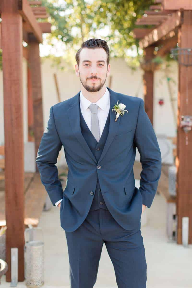 Man in Modern Groom wedding suit with boutonniere poses under gazebo.
