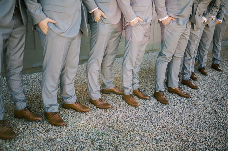Cropped view of men in light-grey suits by Modern Groom lined up on a gravel walkway.