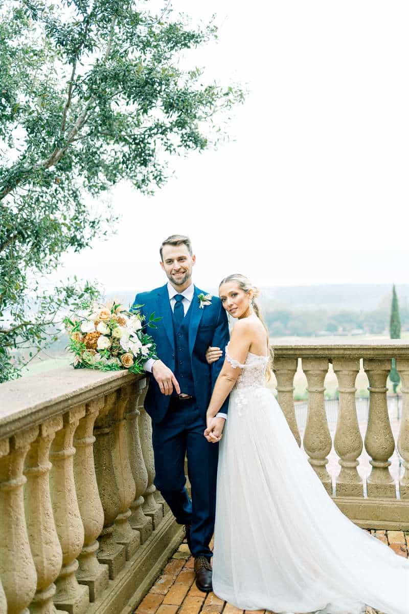 Bride and groom on a balcony with a blue Modern Groom suit and wedding dress.