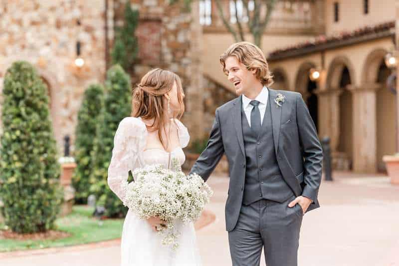 A young bride and groom laugh together in a stone courtyard.