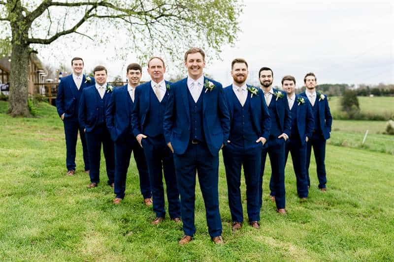 A groom and his groomsmen pose in navy blue suits and boutonnieres.