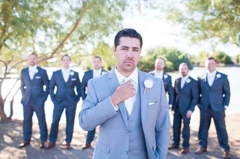 The groom, in a light grey suit, poses in front of his groomsmen wearing dark grey suits.