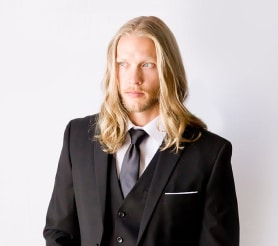 Cropped shot of a male with blonde hair posing in a black suit by Modern Groom.