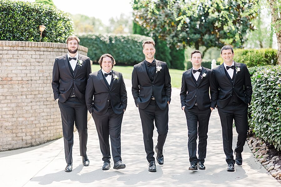 Groom and groomsmen walking in a line on the sidewalk wearing black 3-piece wedding suits
