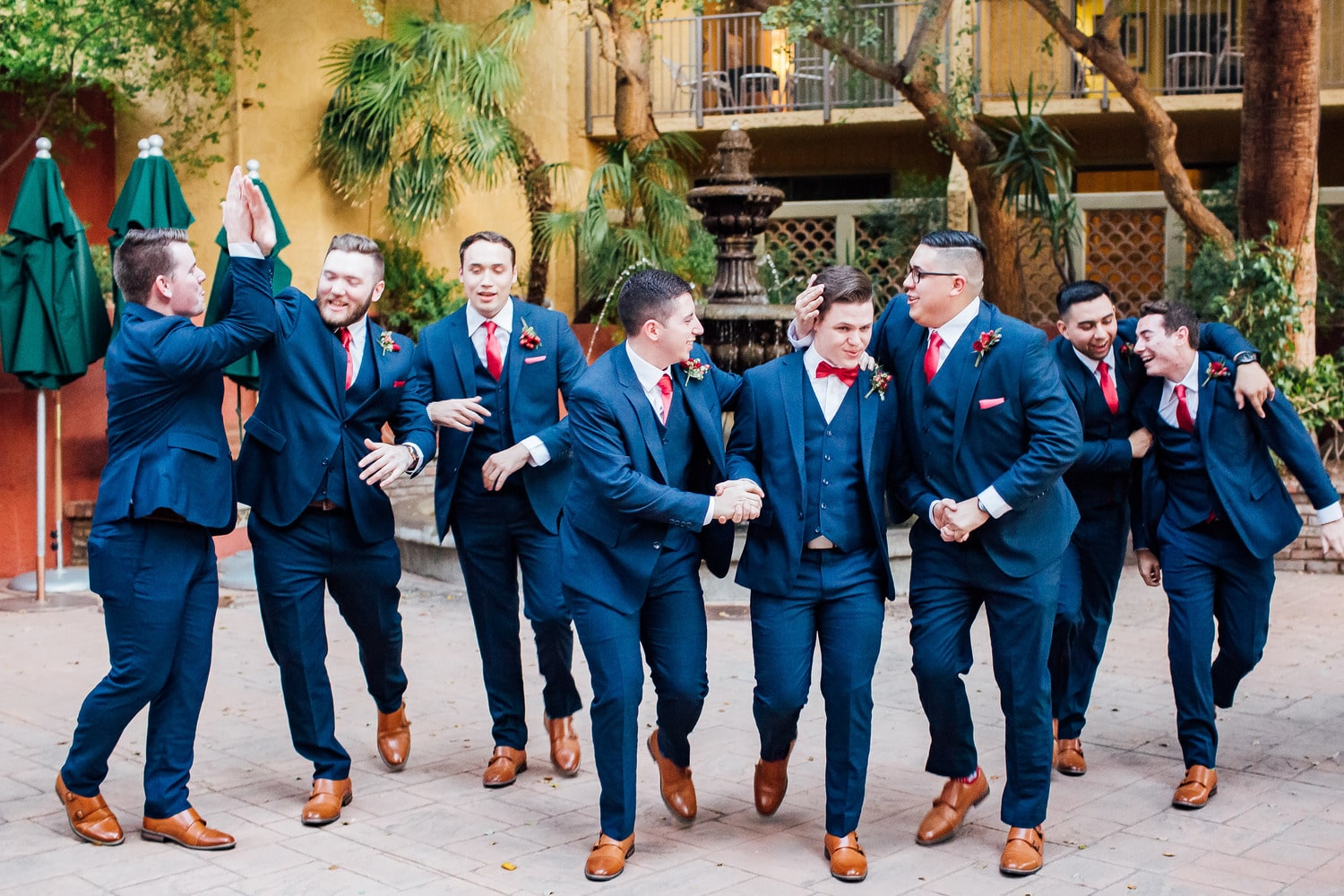 Groom and groomsmen in navy wedding suits laughing and holding each other outside of a yellow building