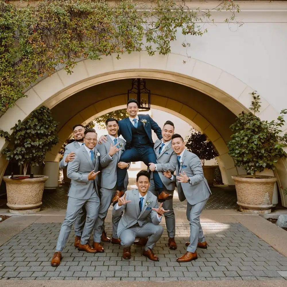 Groomsmen in gray suits carrying the groom in the center wearing a navy blue suit outside