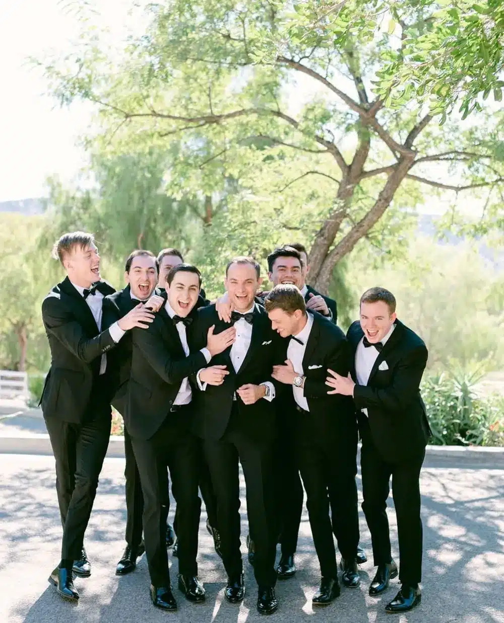 Groom and groomsmen laughing together in matching black suits on the wedding day