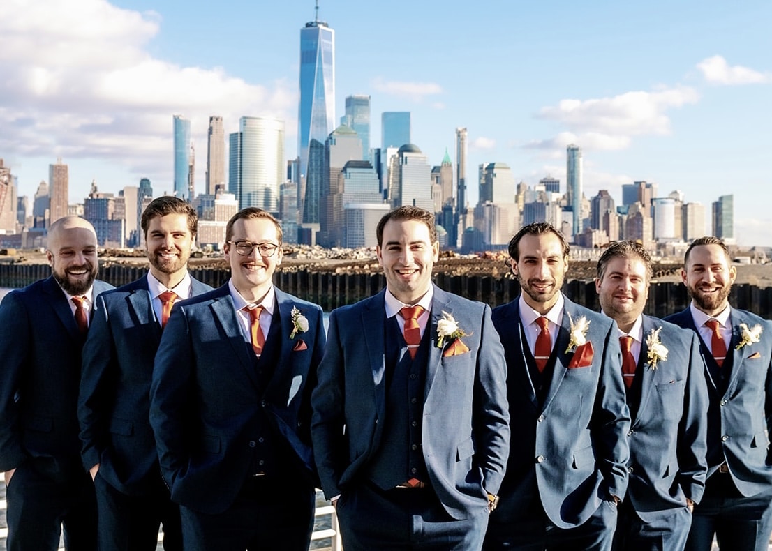 Groom and groomsmen on a boat wearing navy wedding suits with a city skyline in the background