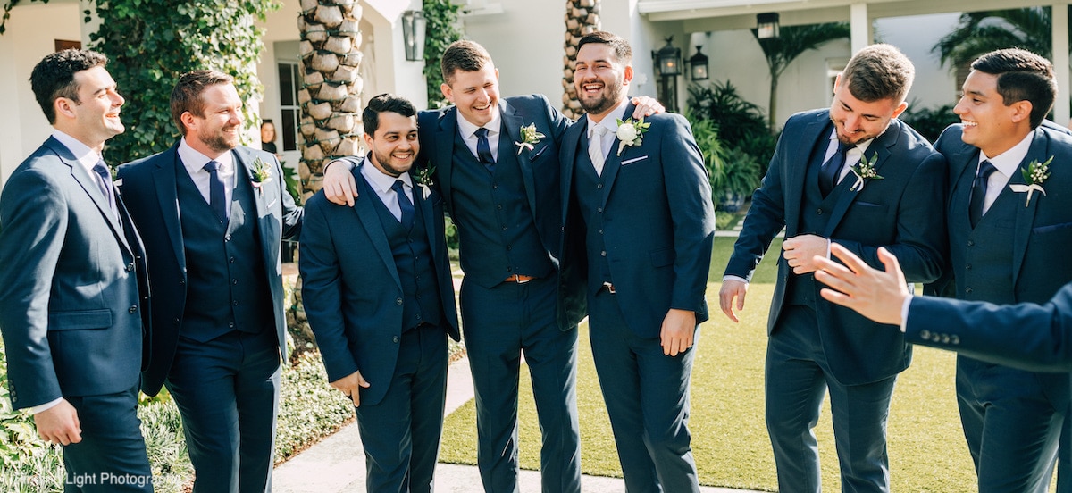 A groom and groomsmen outside of the wedding venue smiling in their navy blue 3-piece wedding suits