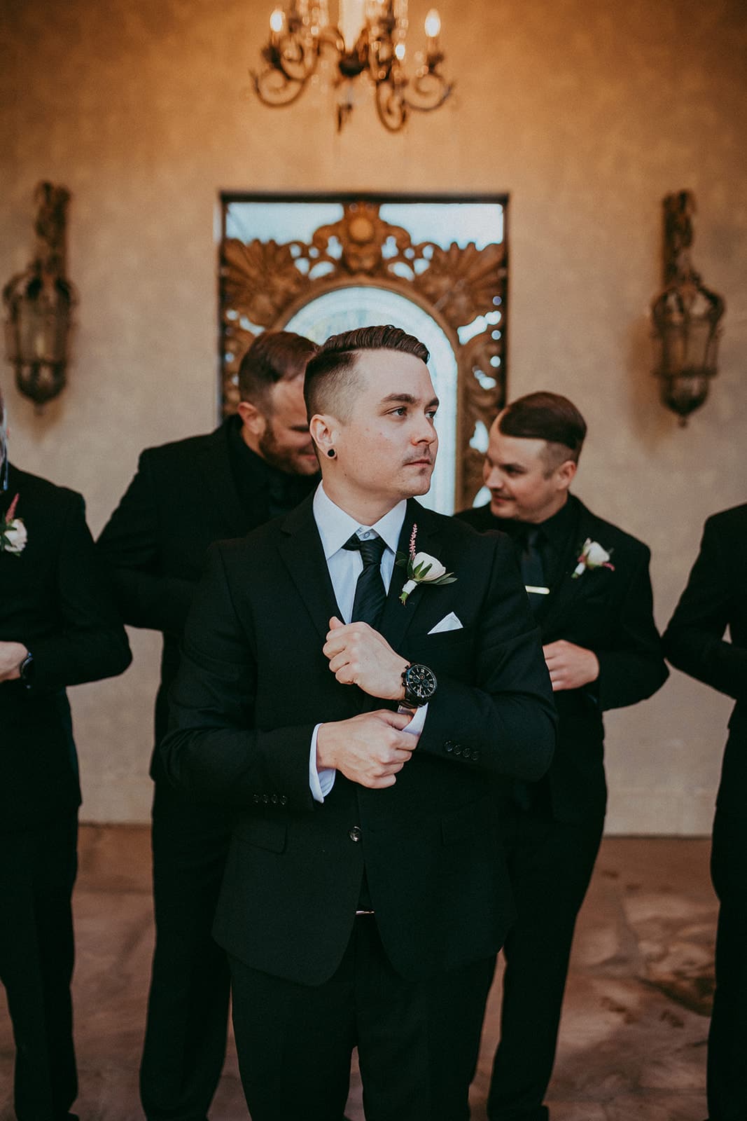 Groom standing in front of groomsmen wearing black suits against a modern art wall and chandelier