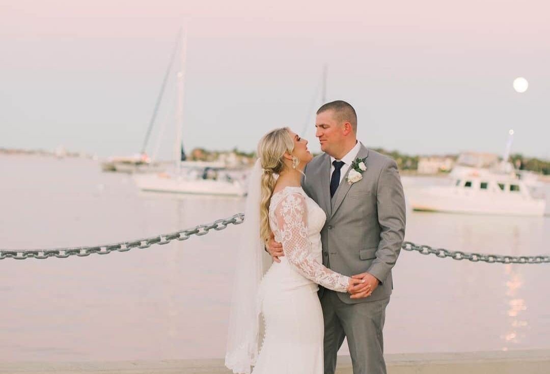 Bride in a wedding dress and groom wearing a grey 3-piece wedding suit posing in front of the ocean