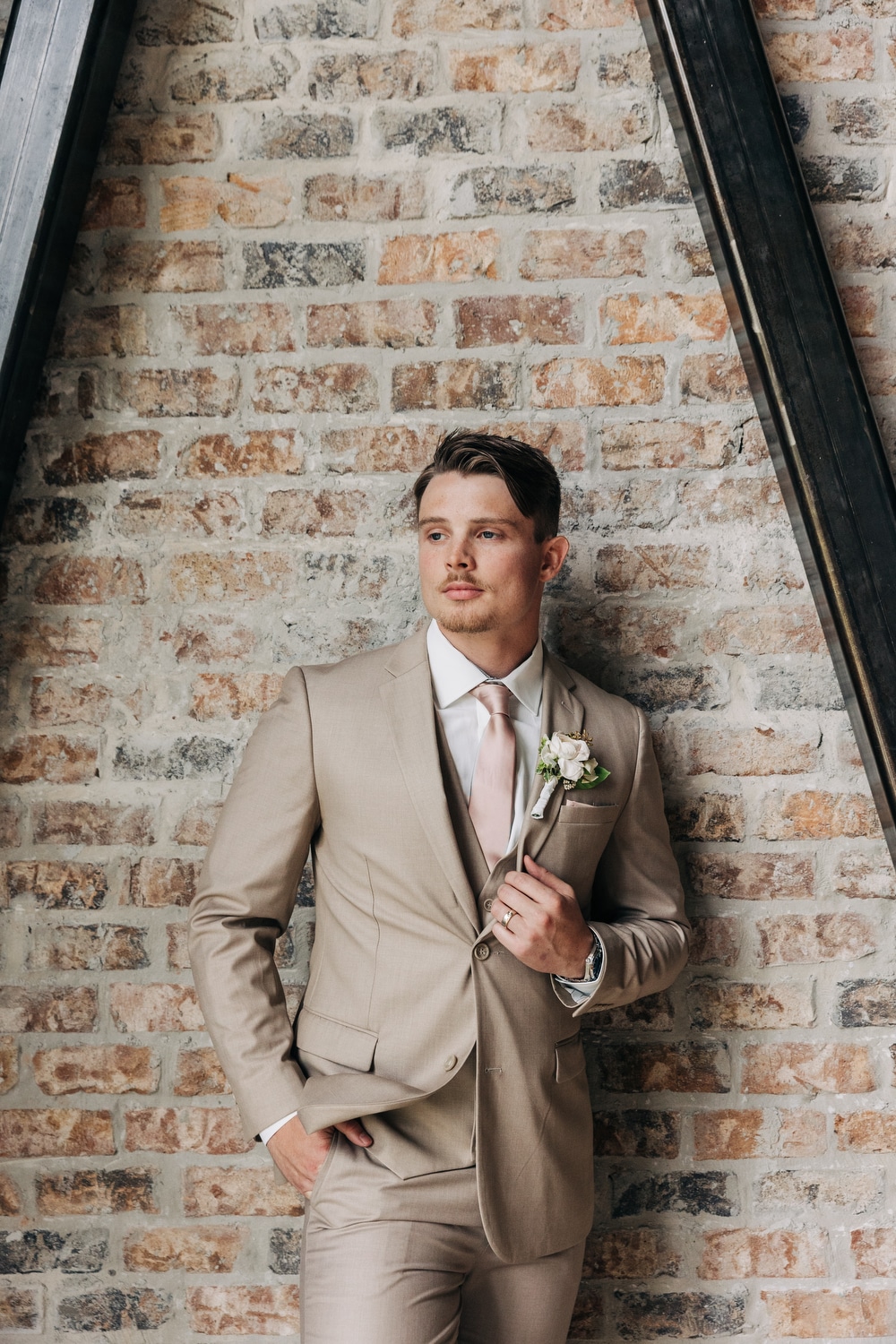 A man shows off his summer wedding suit for grooms while standing against a brick wall