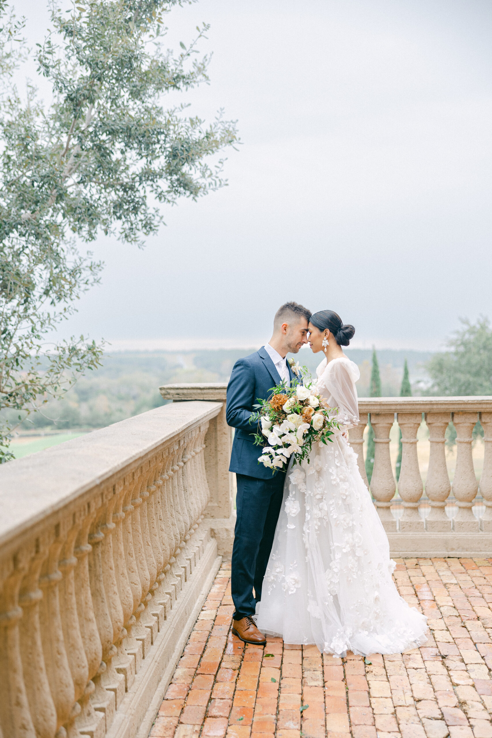 Groom leaning his face into the bride wearing a Heathered Navy winter wedding suit on the balcony