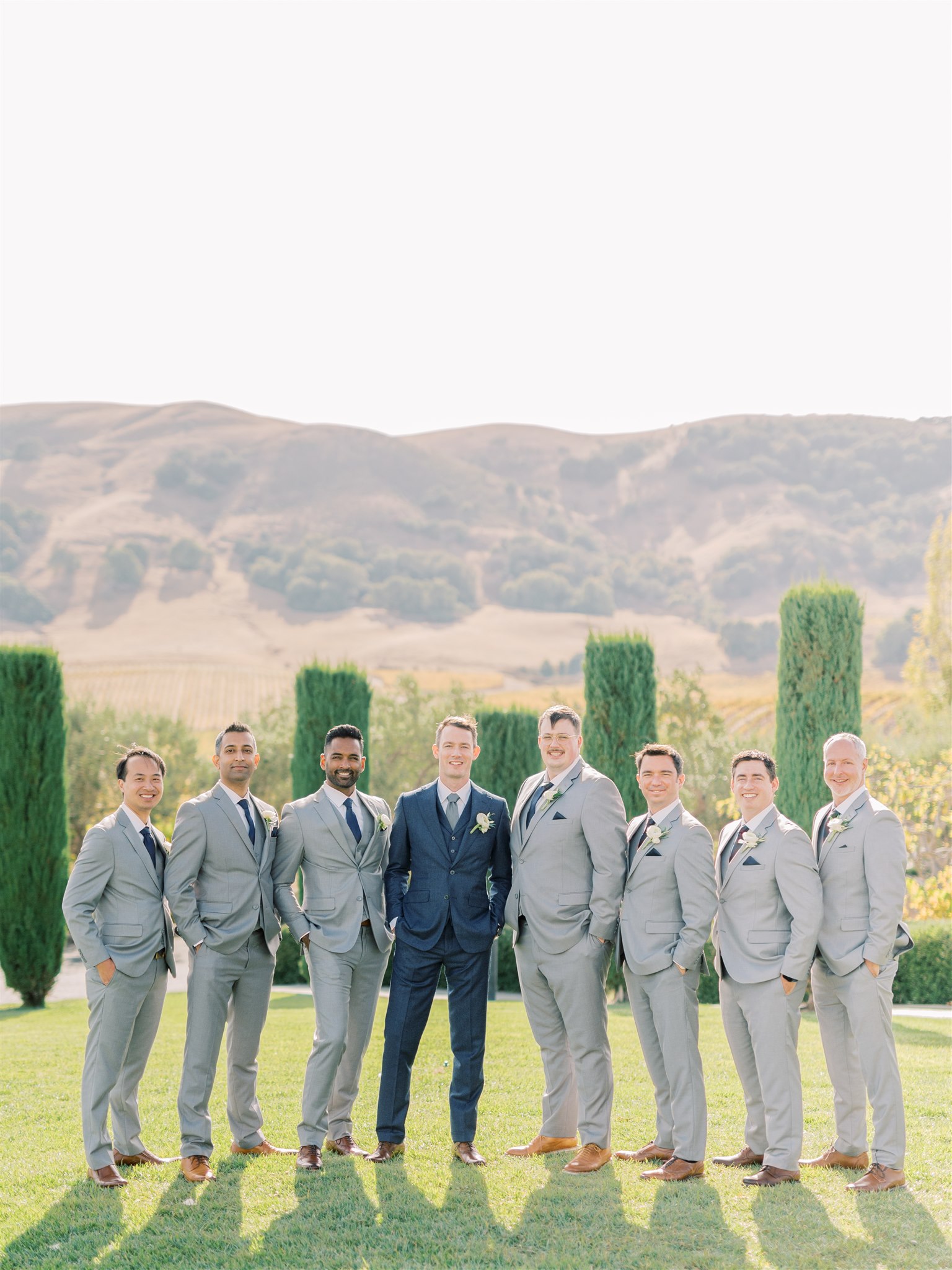 A groom and his groomsmen outside in a spring field posing in spring wedding suit colors