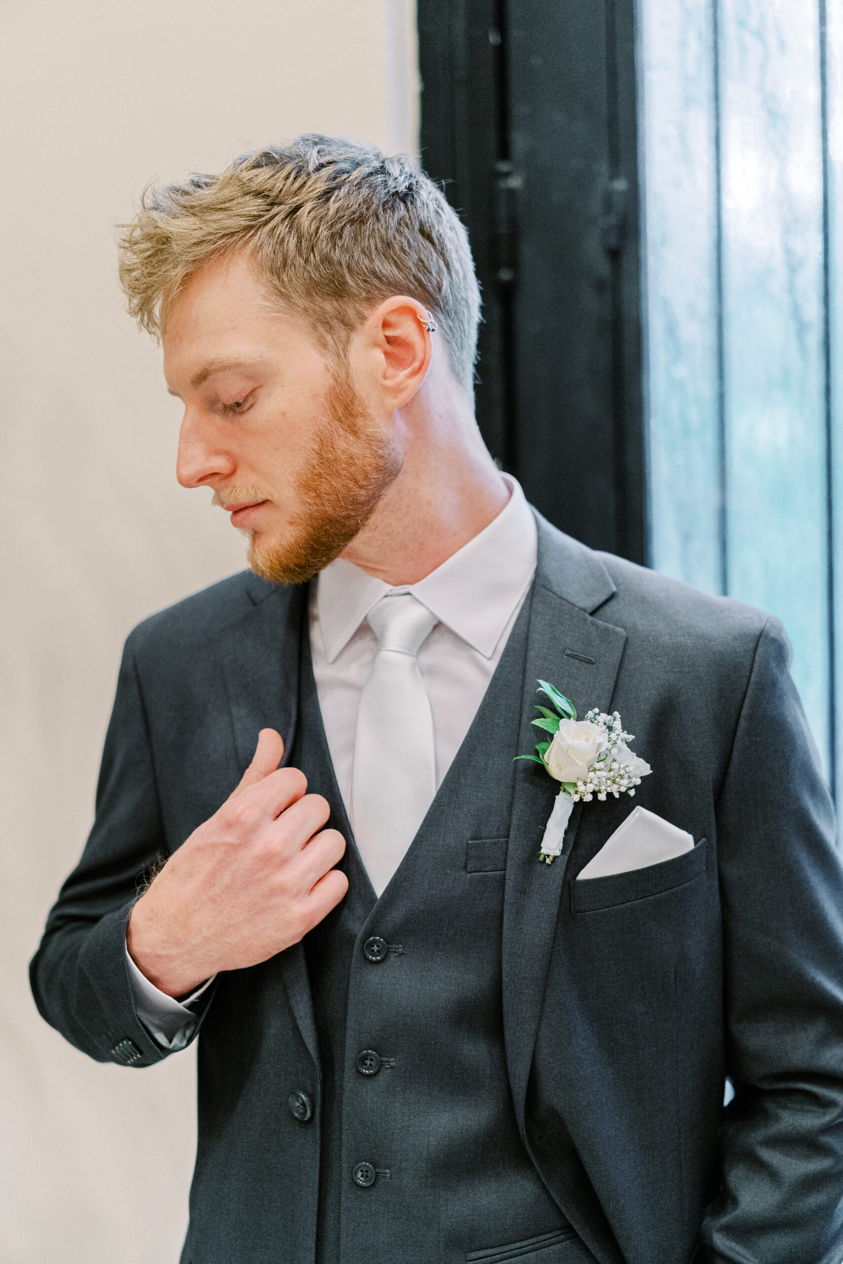 Groom in charcoal fall wedding suit color poses in front of a door