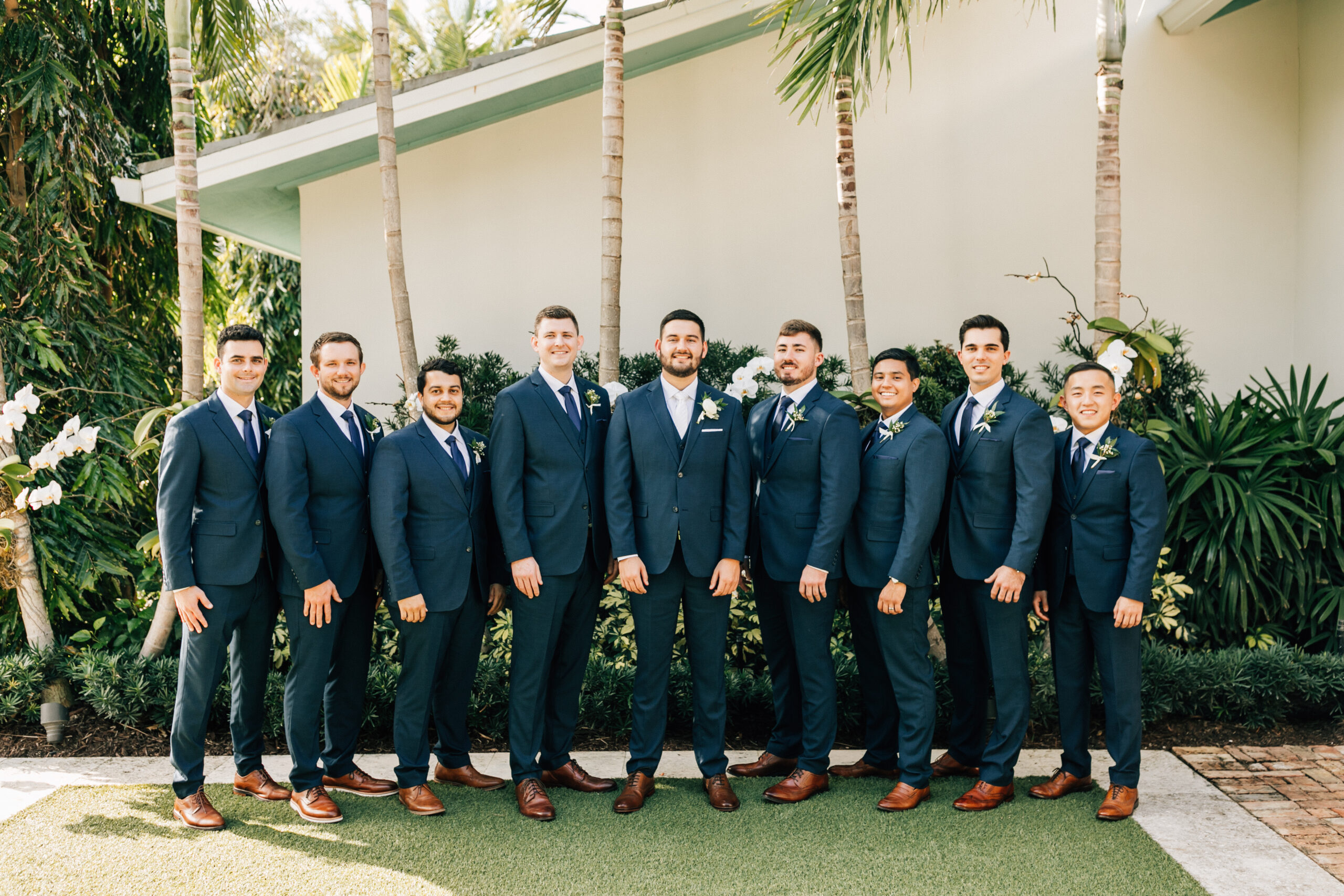 Groom and groomsmen posing outside in greenery wearing matching navy blue wedding suits