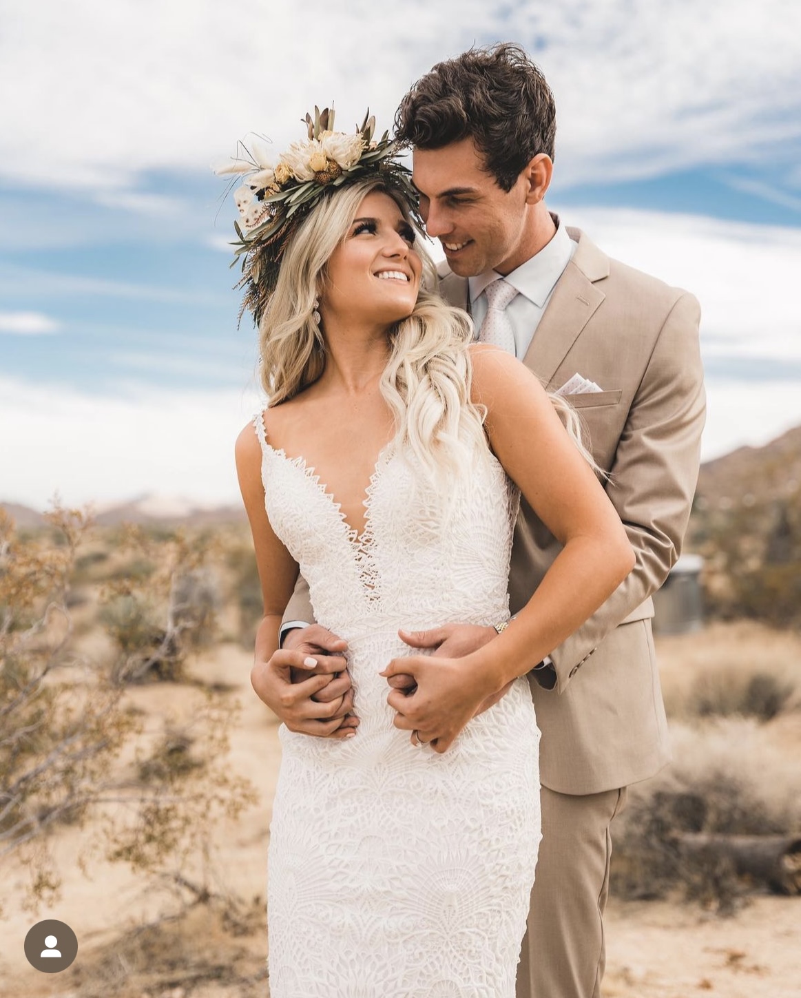 Groom in a tan spring wedding suit holding his bride in a desert field