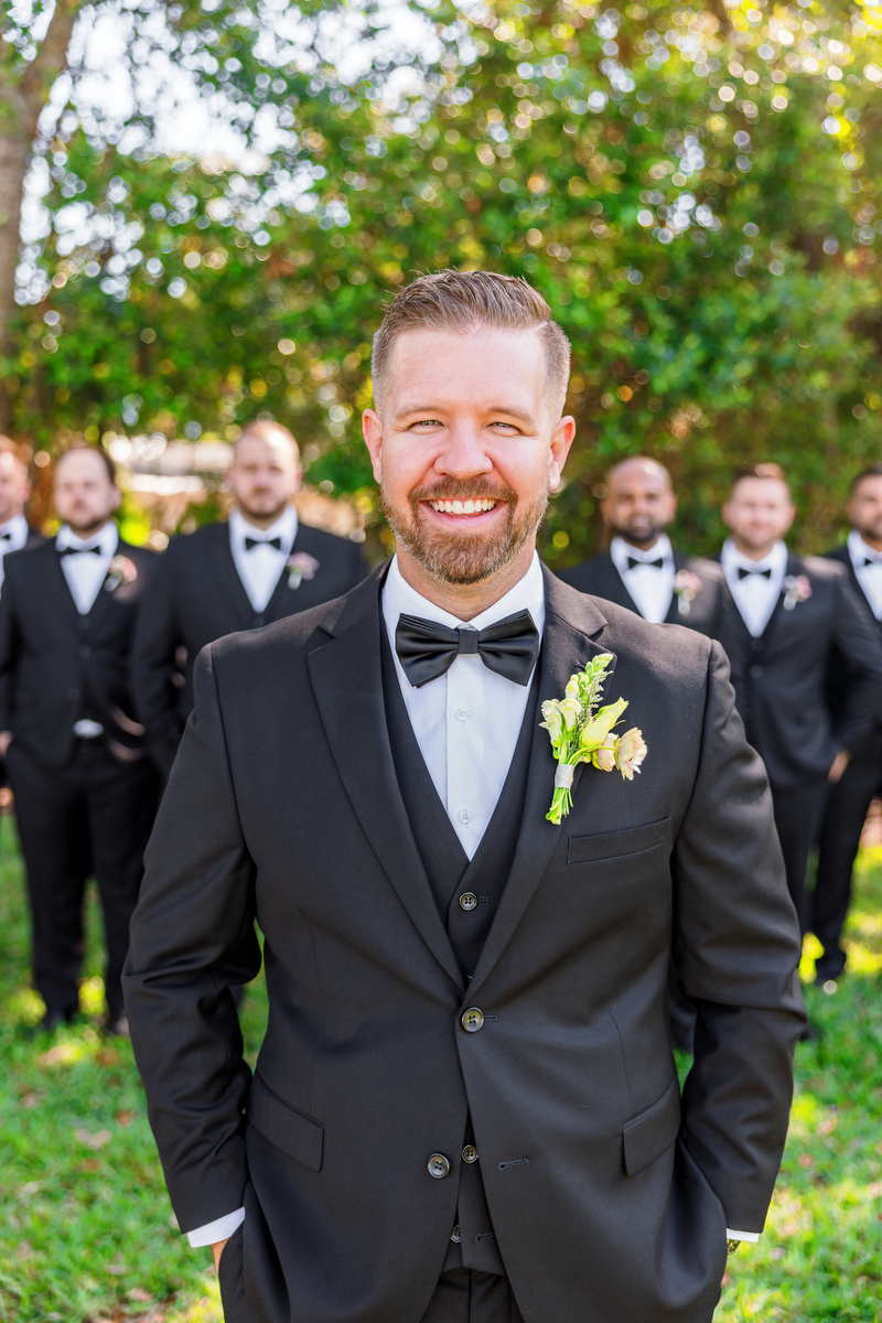 A groom in a 3-piece suit stands in front of the groomsmen