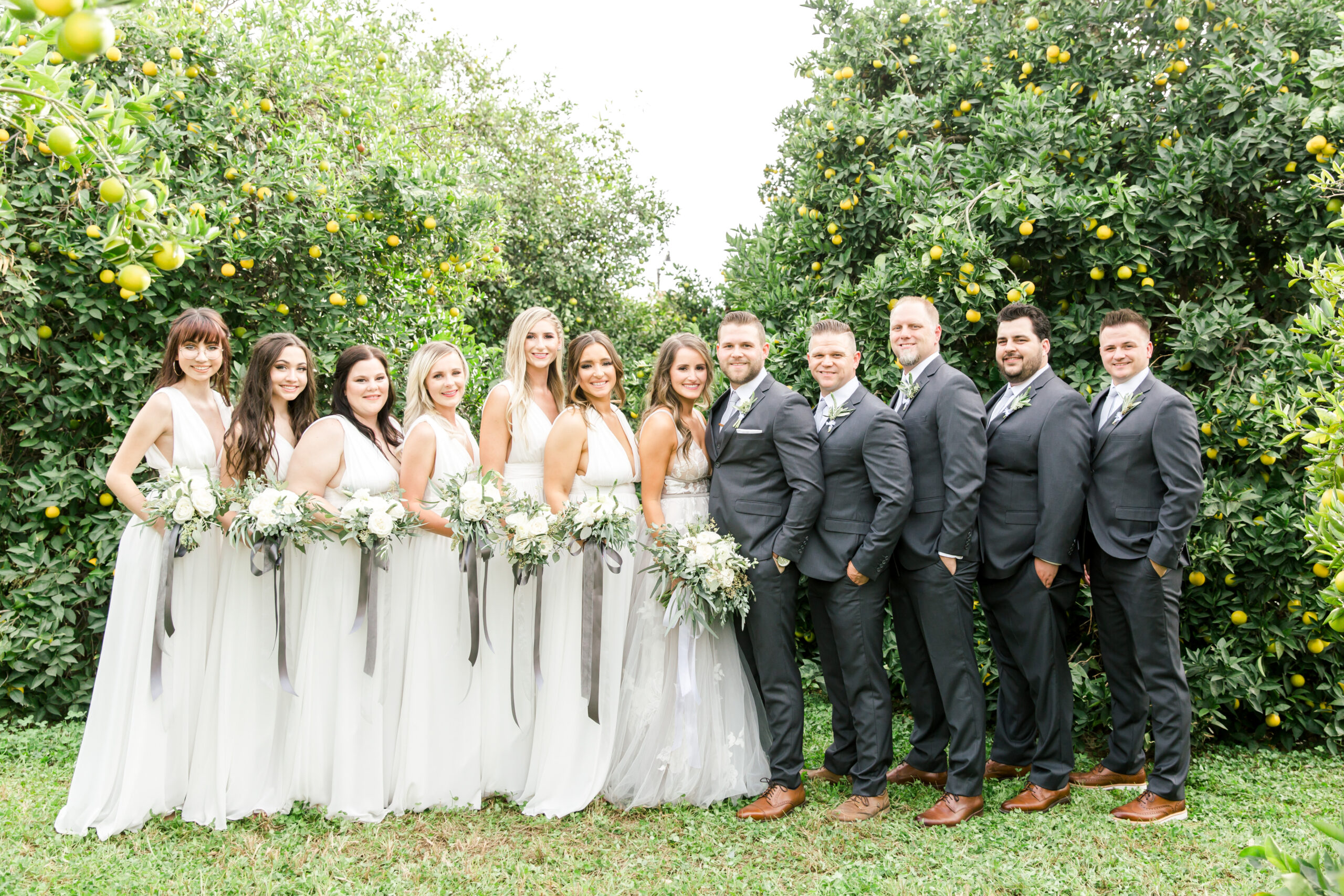 Groom and groomsmen in full frame suits with bride and bridesmaids outside in the greenery