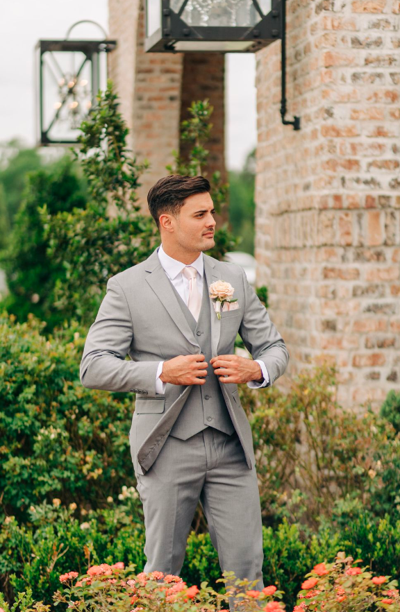 A groom buttons his suit jacket outside