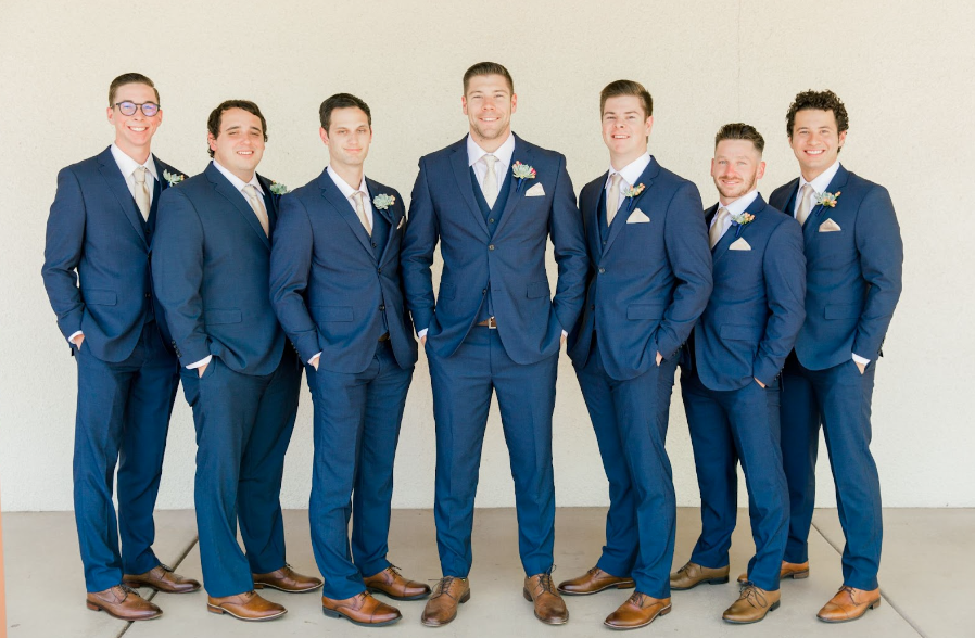 Groom and groomsmen smiling in a line outside in gray big and tall wedding suits