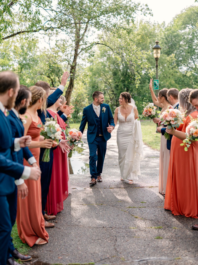 Groom and bride walking down an aisle of bridesmaids and groomsmen in spring wedding outfits