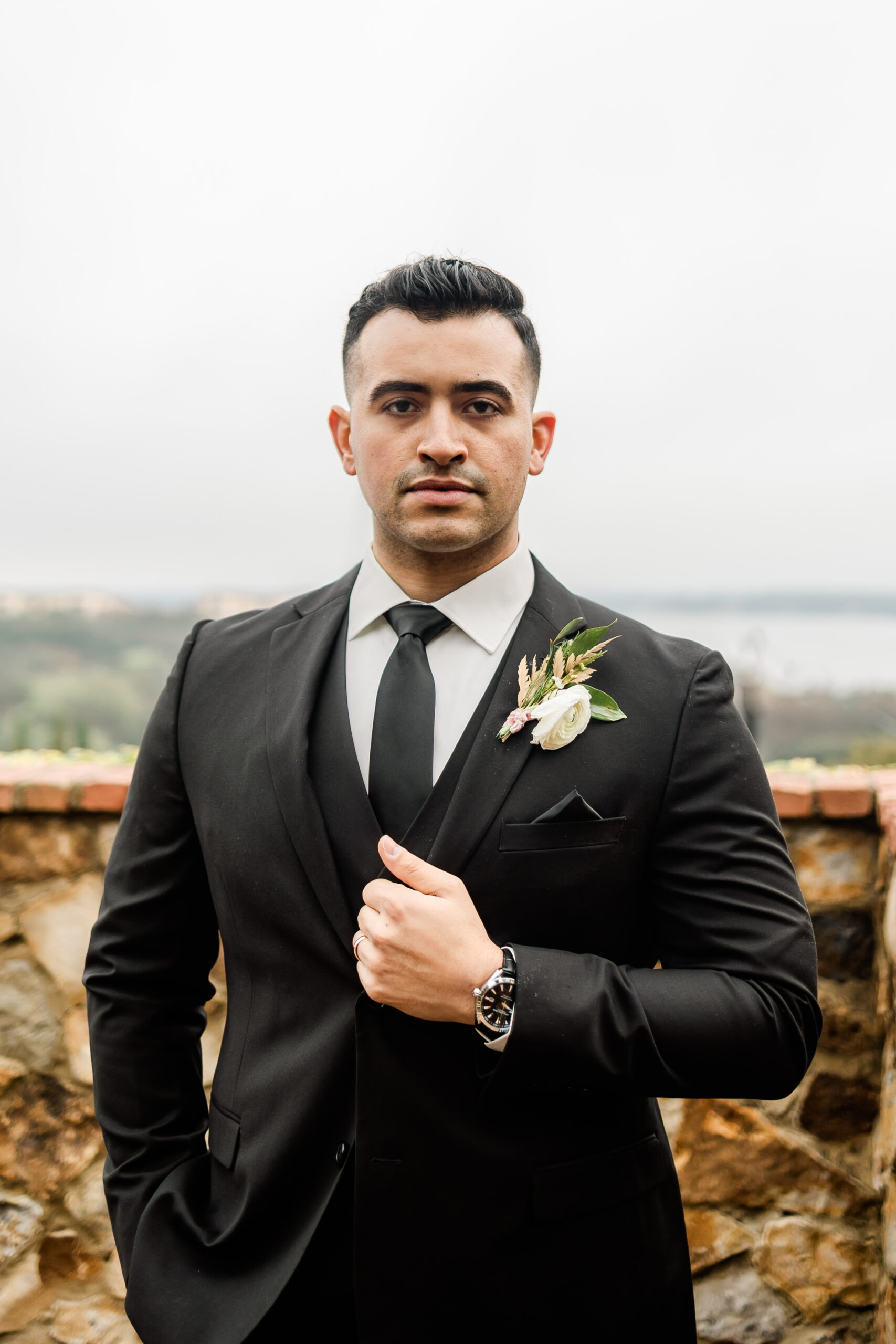 Serious groom wearing a black suit, black tie, and boutonniere for his wedding day