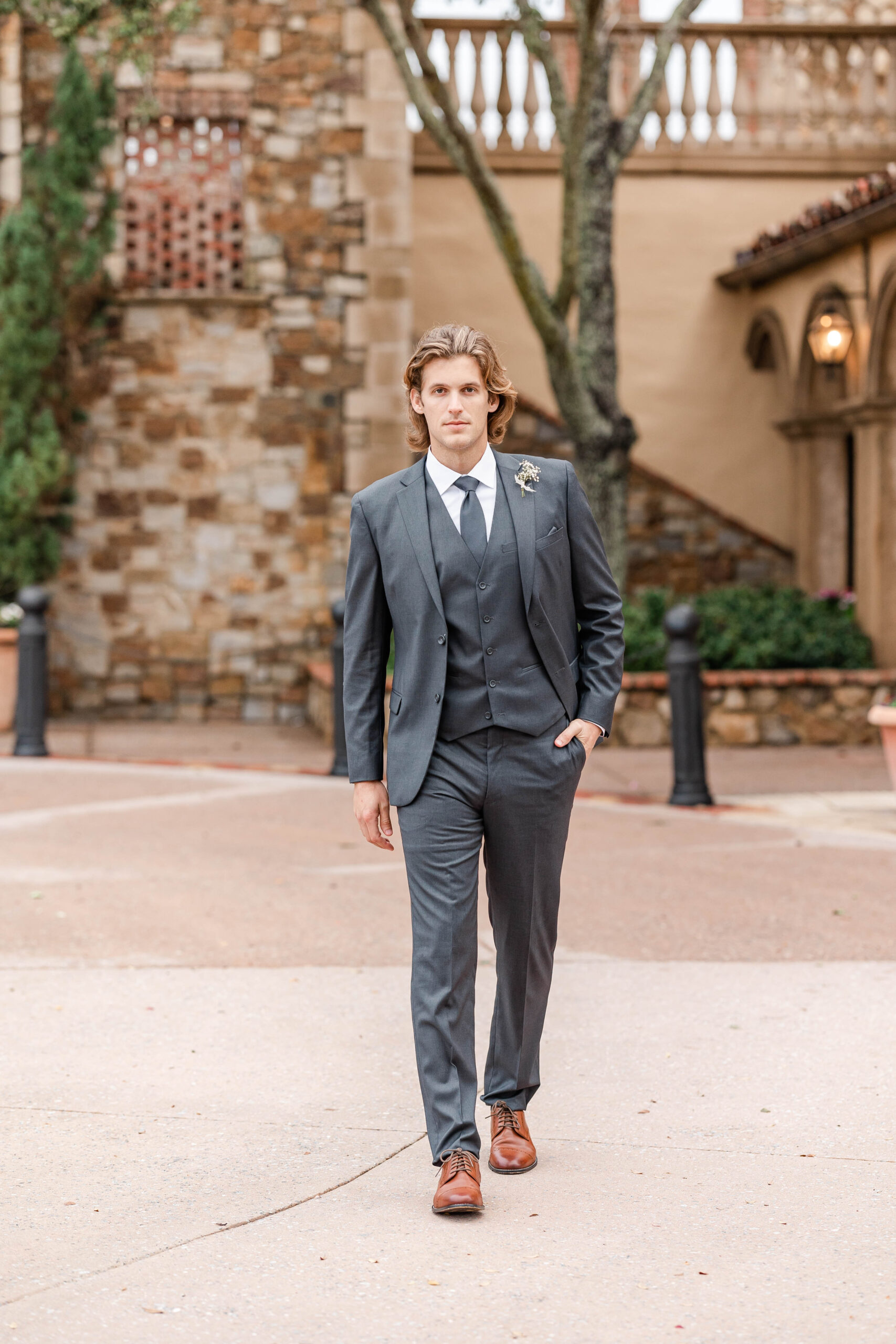 Groom walking in the courtyard wearing a charcoal grey wedding suit