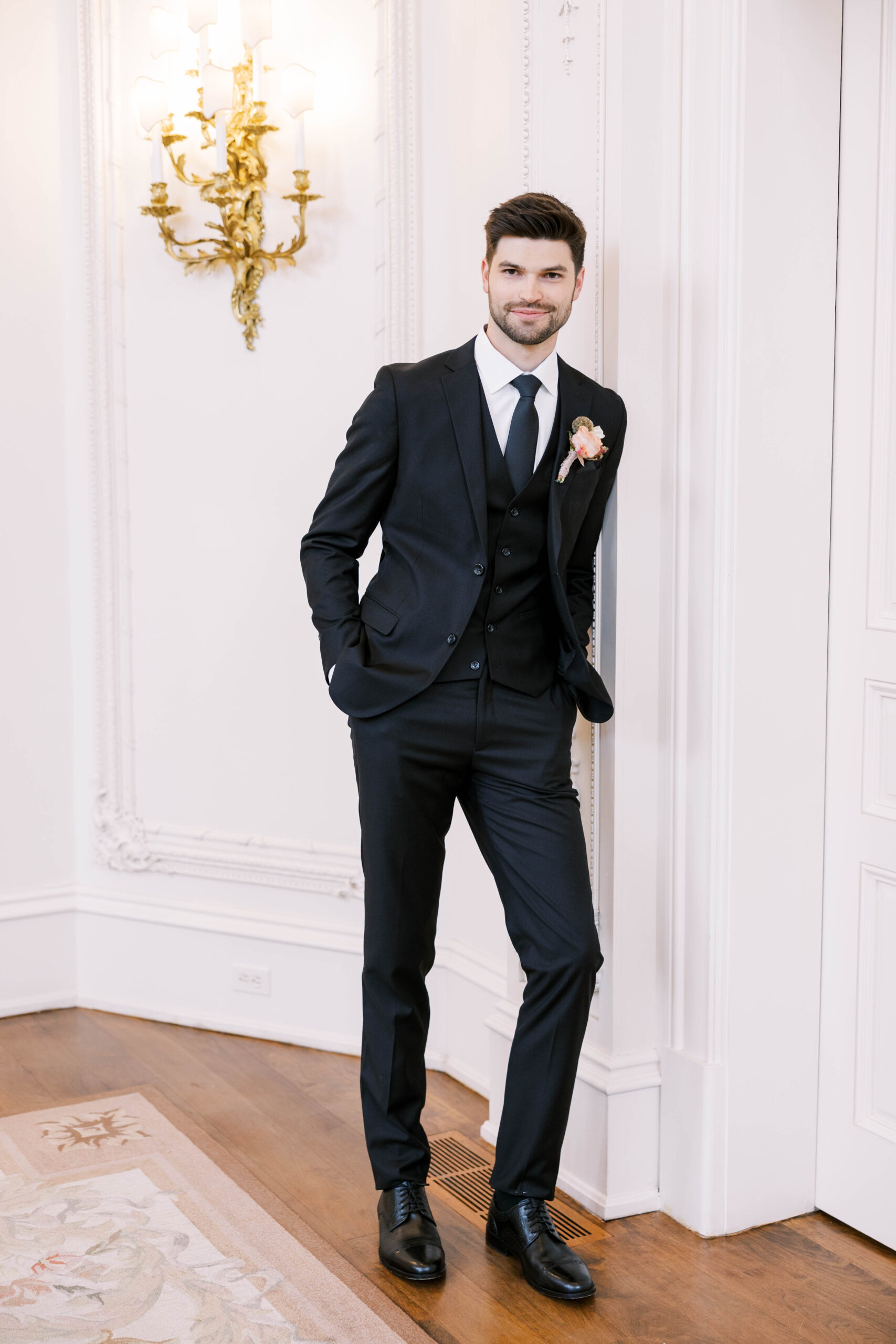 Groom wearing black tall and skinny suits inside of the wedding venue