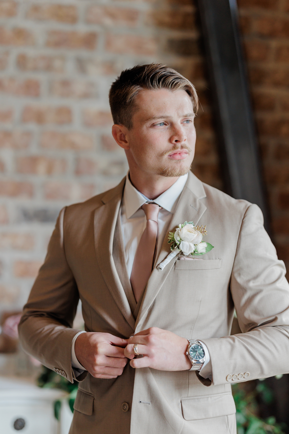 A man buttons up his tan suit jacket with a traditional suit fit
