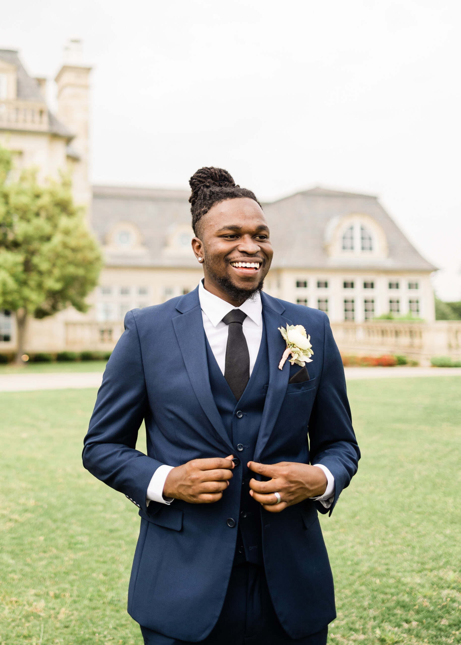 Groom smiling in front of the wedding venue in a navy blue big and tall men’s suit