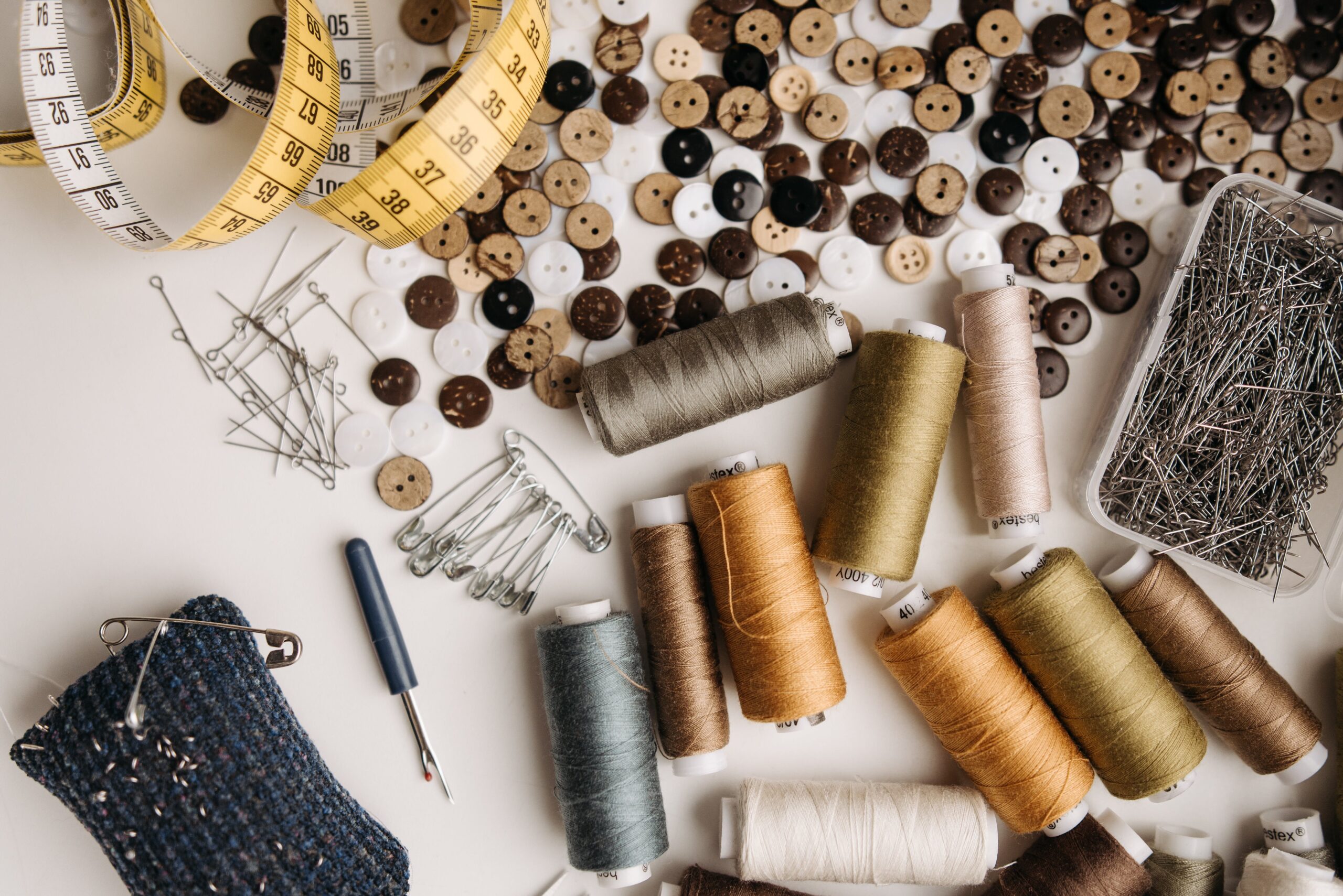 Tape measure, buttons, needles, pins, and spools of thread laid out across of a table for suit alterations