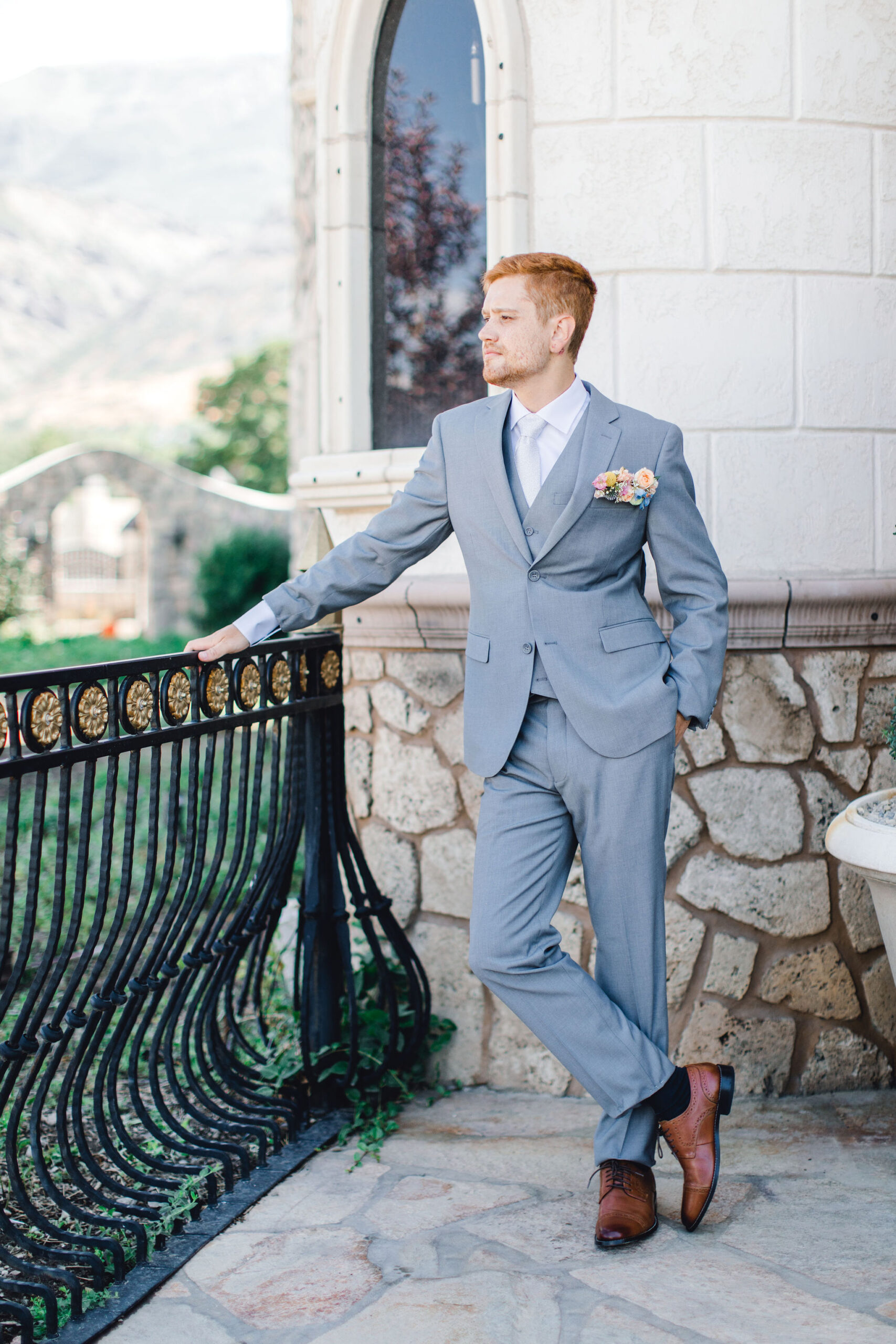 Groom wearing shorter suits for men posing against the railing of a patio