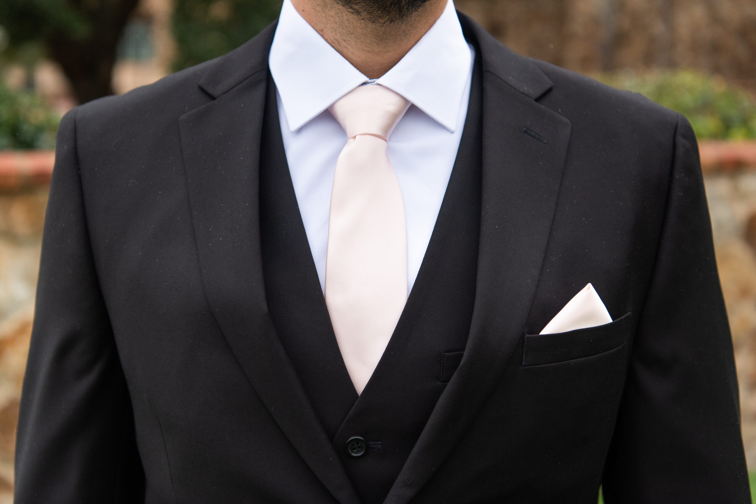 A man wearing a three-piece black suit with a pale pink tie and matching pocket square