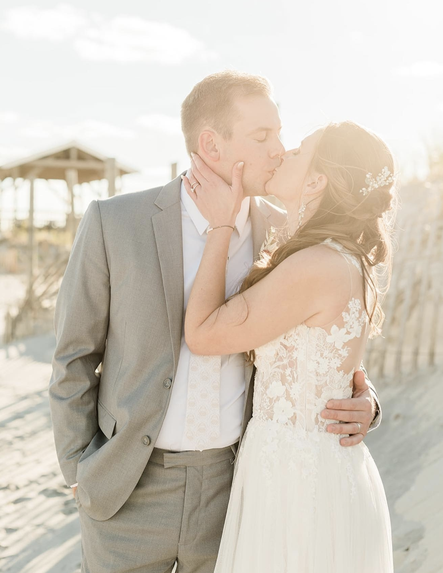 A happy groom and bride kissing on a beach after learning how to travel with a suit and dress
